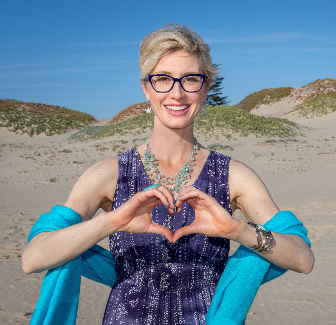 Megan Barnhard on a beach with her hands formed into a heart